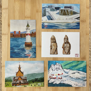 Flat lay of all five postcards in the Norway Postcard Set - Lofoten edition: lighthouse, Oslo Opera House, Viking chess pieces, Heddal stave church, and Lofoten mountains