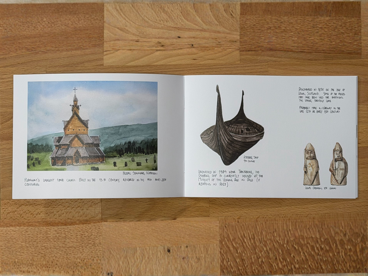 An open printed booklet or book spread laid flat on a wooden surface, showing a watercolor church illustration on the left page and black line drawings with handwritten notes on the right page.